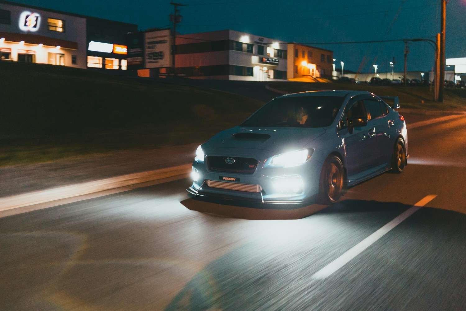 A sleek dark modern car headlight and grill reflecting city lights at night